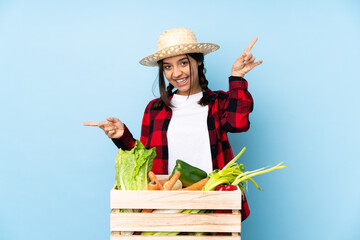 Young farmer Woman holding fresh vegetables in a wooden basket pointing finger to the laterals and happy