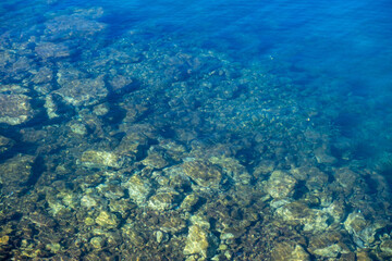 Naklejka na ściany i meble Clear crystal shallow blue sea water and rocky seabed background, high angle view.