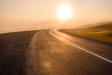 Fototapeta na wymiar Deserted winding mountain pass shrouded in fog at sunset. Lens flare.