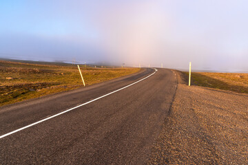 Empty winding mountain road covered with fog at sunset