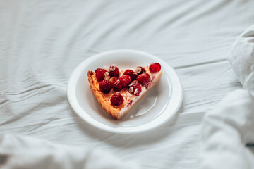 Piece of classic cheesecake with raspberry berries on a white plate on the bed.