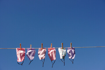 pink and purple cloth face masks on close line in sun on blue background with copy space 