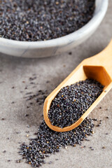 Poppy seed in wooden spoon with bowl on stone background.