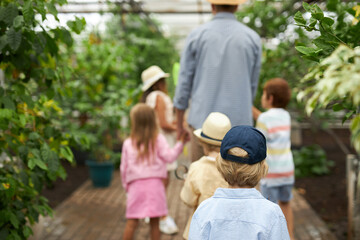 group of children walk in greenhouse with teacher man, he talks about nature, tells how the world around was created and who lives and grows in it