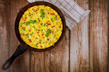 Homemade omelette with vegetables in pan on wooden background.