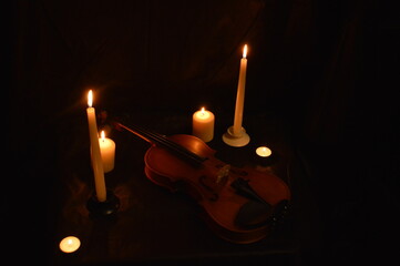 Group of burning candles and violin on black background.
