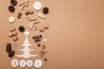 Festive Christmas composition in eco style of fir and pine cones, walnuts, macadamia, peanuts, cinnamon sticks, wooden decorations and numbers 2021 on a beige background.Christmas and New year concept