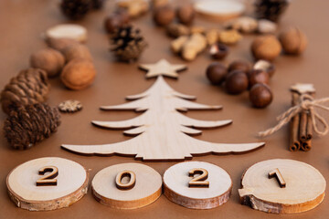Fototapeta na wymiar Festive Christmas composition in eco style of fir and pine cones, walnuts, macadamia, peanuts, cinnamon sticks, wooden decorations and numbers 2021 on a beige background.Christmas and New year concept