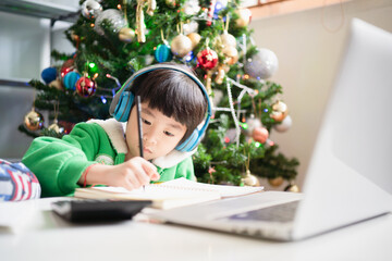 Asian boy wearing headphone and using laptop while learning online from home which have blur of...