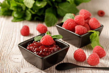 Raspberry jam marmalade in dark bowl with fresh berries and mint leaves