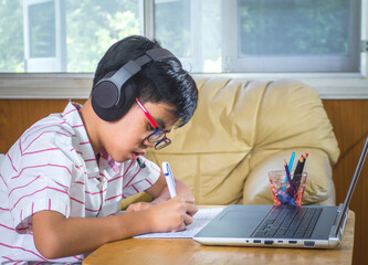 The boy wearing headphones sitting at the table with internet chat skype teacher prepare for exam...
