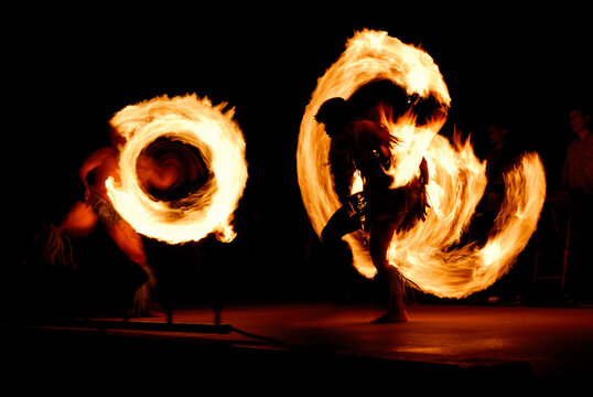 Pair of competing fire dancers spinning lit batons at night after a luau