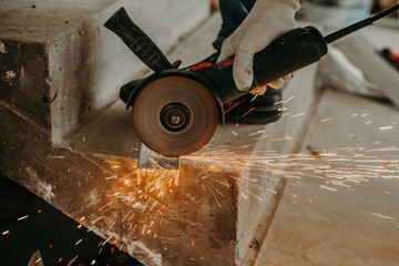 A worker cuts off a piece of metal with a electric grinder - obrazy, fototapety, plakaty