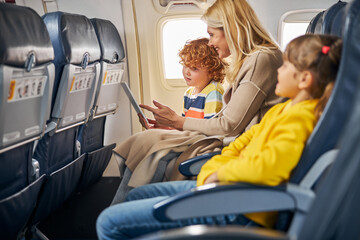 Woman inside a plane showing a tablet to a boy
