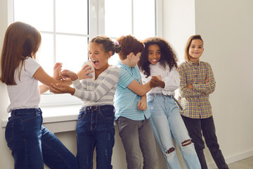 Active group of multiethnic children have fun together and tickle each other standing by the window.