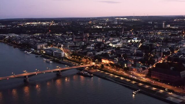Approaching the City of Mainz in Rheinland Pfalz with a drone at magic hour with all the city lights showing the old bridge an the Rhine river
