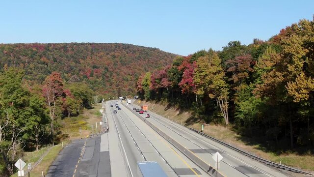 Rising aerial above highway. Beautiful autumn fall foliage as traffic snakes through deserted hillside mountain area on interstate turnpike road.