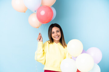 Woman holding balloons in a party over isolated blue background