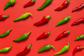 Hot red and green fresh chili peppers on red background flat lay top view. Seasoning for dish, spicy spices for cooking, cayenne pepper, food. Creative layout, chili pattern