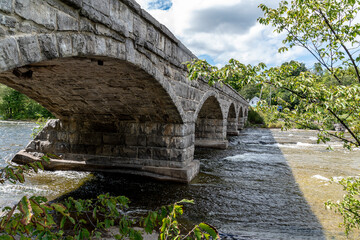 The historic Pakenham five-arch stone bridge in Pakenham, Ontario crosses the Mississippi River on a partially cloudy day.