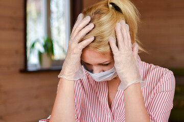 Headache in a woman. A woman in a medical mask and gloves holds her head.