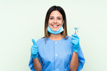 Woman dentist holding tools over isolated green background giving a thumbs up gesture