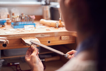Fototapeta na wymiar Close Up Of Female Jeweller Working On Ring With File In Studio