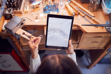 Overhead View Of Female Jeweller Comparing Ring With Drawn Design On Digital Tablet In Studio