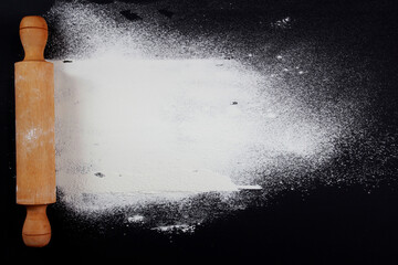 cake roller and flour on black table background