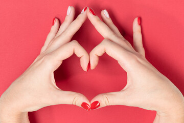 Beautiful hands of a young woman making sign Heart by fingers on red background. Female hands...