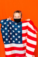 Attractive little boy with the flag of the United States, showing victory on a orange background