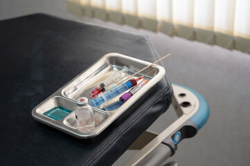 Medical instrument with syringe, vaccine, coronavirus sample blood test tube in tray on patient examination table at lab