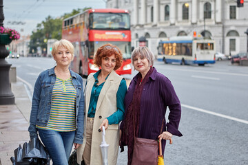 Middle-aged women stand near double decker bus outdoor.