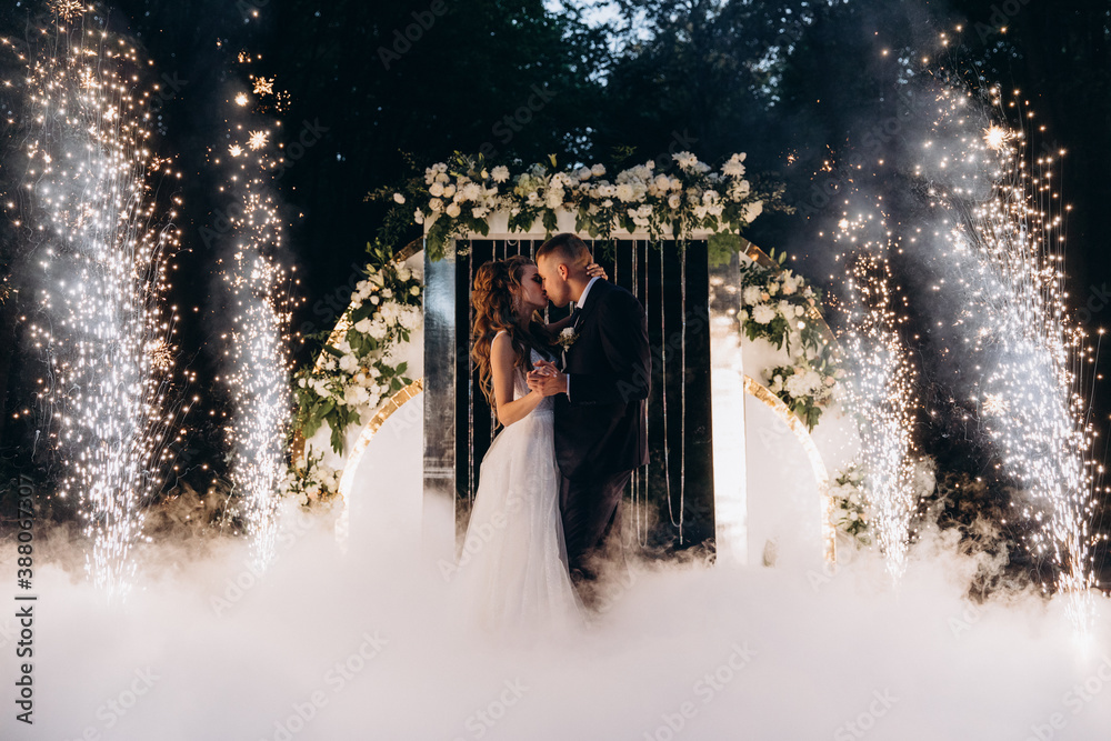 Wall mural Newlyweds on the background of the wedding arch. Night fireworks.