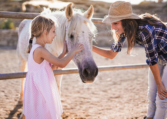 Happy mother and daughter caress horse outdoor at ranch - Mom and child - Animal love