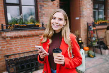 Cheerful young caucasian woman wearing coat walking with coffee cup. Can use for holiday halloween concept