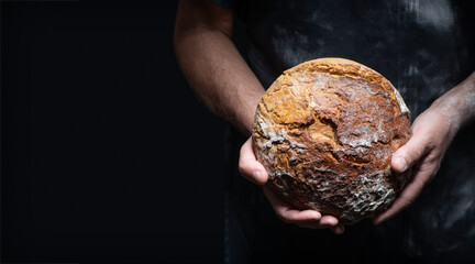 Baker's hands holding and presenting fresh baked loaf of bread