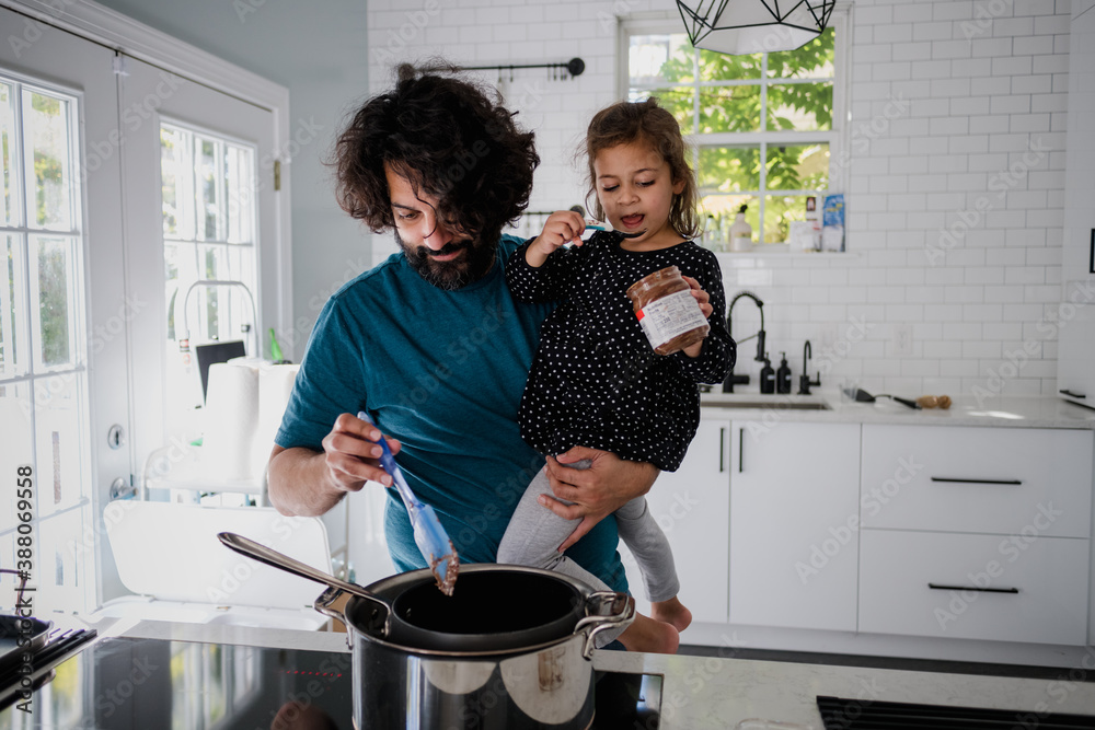 Wall mural father holding daughter while cooking on stove top in modern kitchen