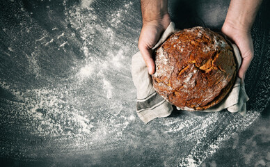 Baker's hands holding and presenting fresh baked loaf of bread - obrazy, fototapety, plakaty