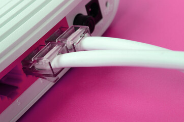 The Internet cable plugs are connected to the Internet router, which lies on a bright pink...