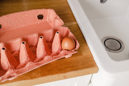 Close-up View Of A Single Raw Chicken Egg In Egg Box On A Kitchen Wooden Counter