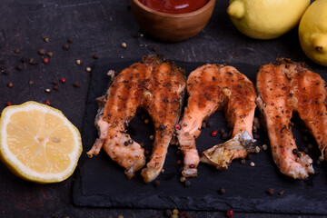 Grilled fresh salmon steak with pepper and lemons on dark table. Fish for healthy food