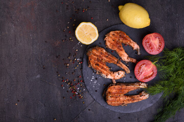 Grilled fresh salmon steak with pepper and lemons on dark table. Top view.  Fish for healthy food.