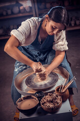 Charming potter master woman works with clay on a potter's wheel. Hand work.