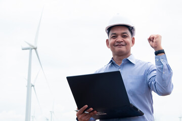 Engineers windmills wearing face mask and  working on laptop with the wind turbine in background