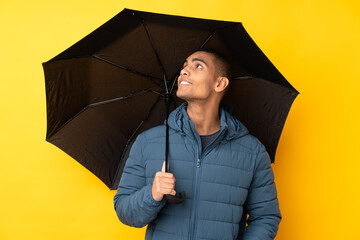 Young handsome man holding an umbrella over isolated yellow background with happy expression