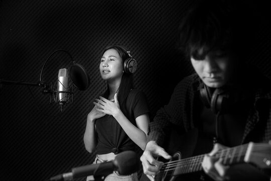 Lady vocalist singing with her guitarist in front of microphone
