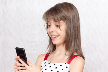 Fototapeta premium Cheerful little girl watches entertainment materials in her smartphone.