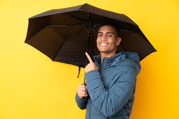 Young handsome man holding an umbrella over isolated yellow background and pointing it