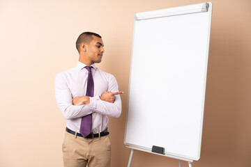 Young business man over isolated background giving a presentation on white board and pointing it